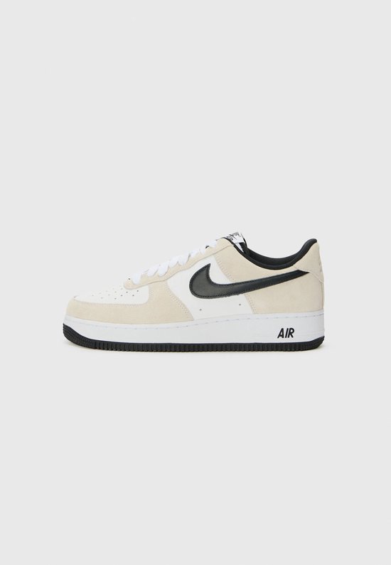 Witte sneaker met beige suède overlays, zwart Swoosh-logo en "AIR" op de zool.