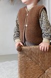 Kind draagt bruin wollen vest met bruine biezen en twee knopen over een shirt met luipaardprint.