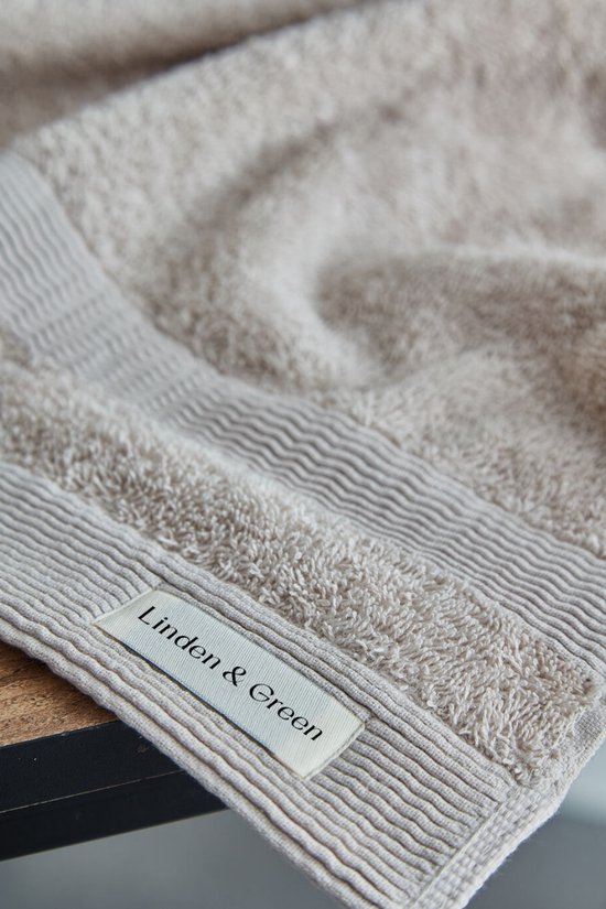 Close-up van de zijkant van een lichtbruine handdoek met een label 'Linden & Green'.