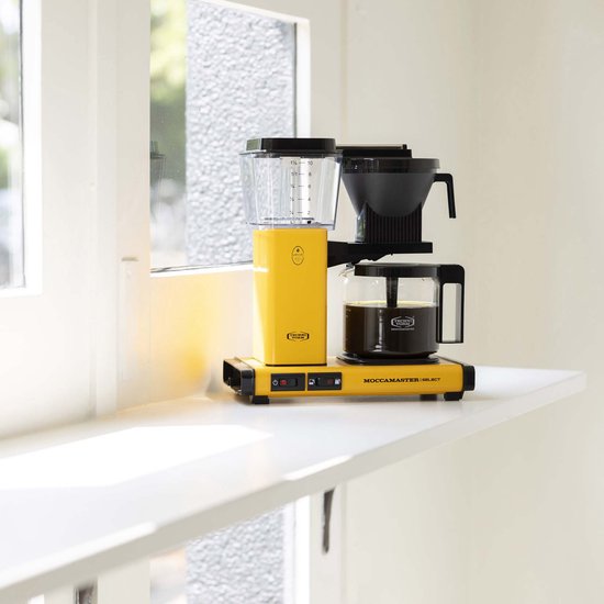 Felgeel Moccamaster koffiezetapparaat met glazen kan gevuld met koffie, op een witte vensterbank.