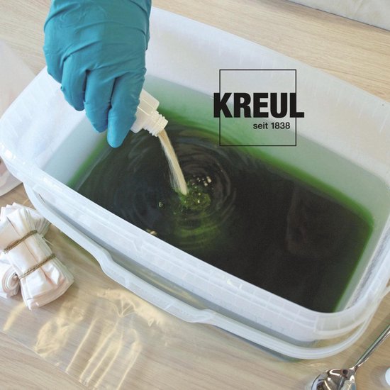 Main avec gant bleu ajoutant du liquide à une cuve de peinture verte et de textile.