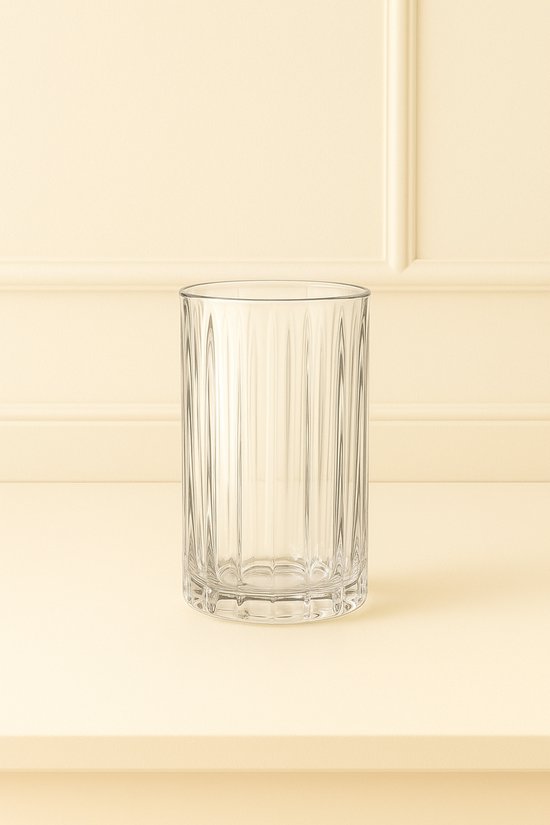 Un verre transparent avec des côtes verticales sur un fond jaune pâle.