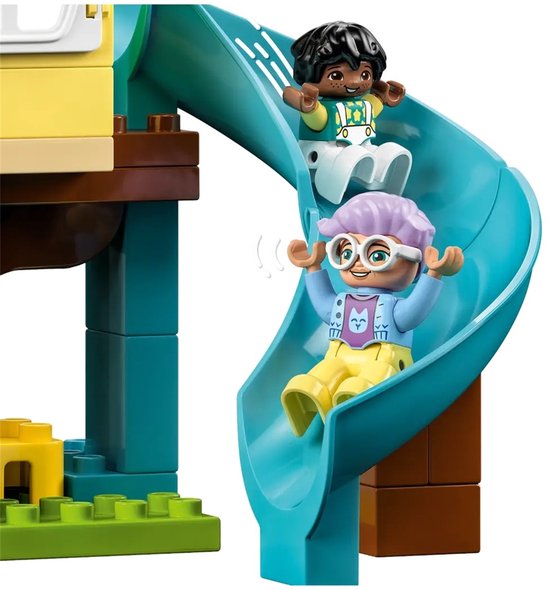 Twee LEGO Duplo poppetjes glijden van een blauwe glijbaan in een boomhut.