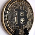 Gouden Bitcoin munt met zwarte details, hangend aan een witte muur.