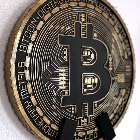 Gouden Bitcoin munt met zwarte details, hangend aan een witte muur.