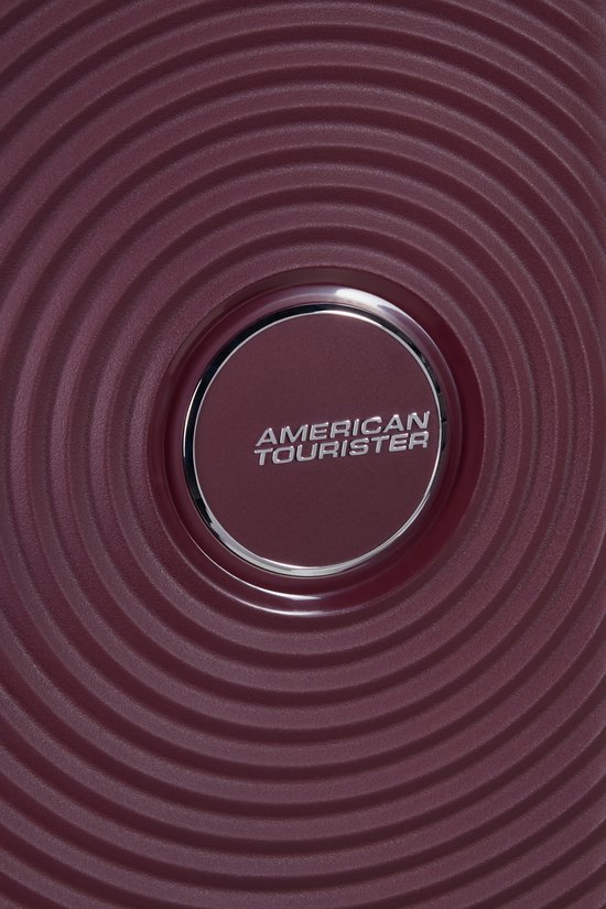 Bordeauxrode koffer met cirkelvormige textuur en zilverkleurig American Tourister logo in het midden.