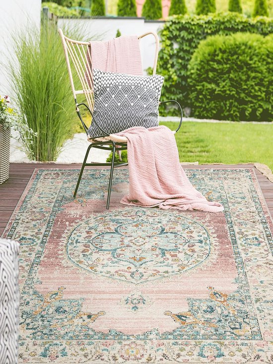 Tapis vintage rose dans un jardin sur une terrasse en bois, avec une chaise avec plaid et coussin roses.