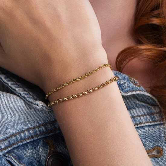 Gouden schakelarmbanden om de pols van een vrouw met rood haar, in een spijkerjasje.