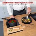 Man gebruikt zwarte inductiebeschermers met ruitpatroon als onderzetters voor pannen met eten op een houten aanrecht.