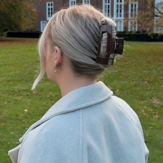 Bruine haarklem met open rechthoek in geblondeerd haar, gedragen met een lichtgrijze jas.