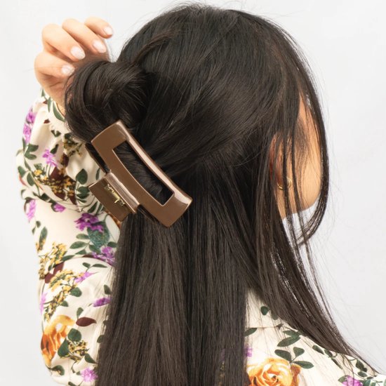 Bruine haarklem met open rechthoek in lang zwart haar, gedragen met bloemenblouse.