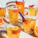 Un groupe de verres avec des boissons jaunes et des bords de sucre rouge.