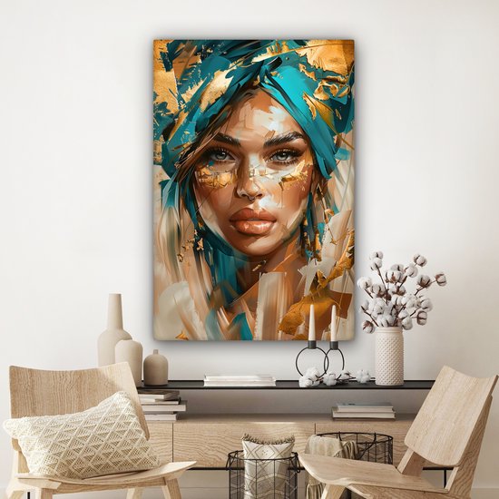 Schilderij van een vrouw met blauwe tulband en gouden accenten, aan een witte muur boven een dressoir.