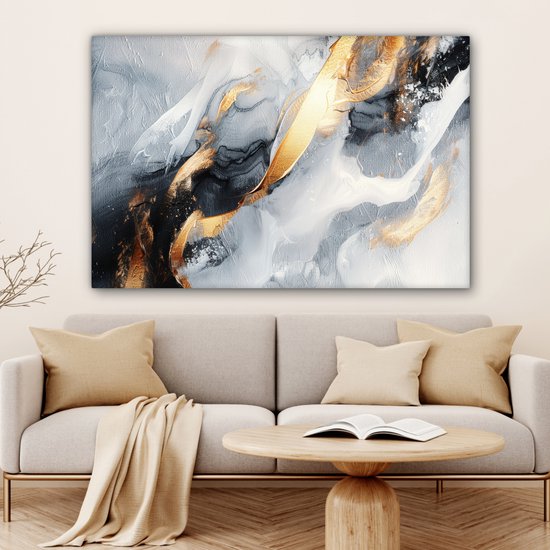 Abstract schilderij met goud, grijs en wit, hangend boven een bank met beige kussens en een plaid.