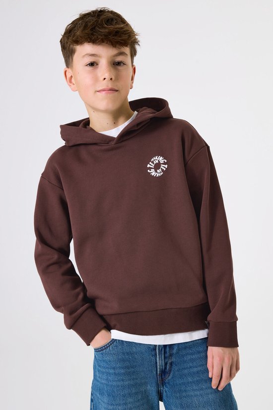 Jongen draagt bruine hoodie met cirkelvormige print op de borst en blauwe jeans.
