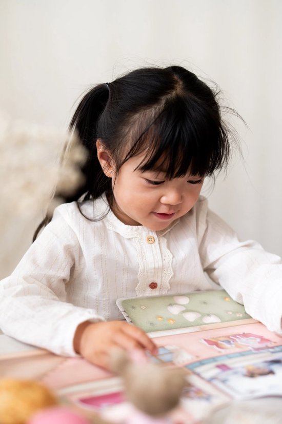 Jong meisje met staartjes en een witte blouse, kijkend naar een stickerboek.