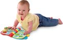Baby in geel shirt en spijkerbroek ligt op de buik, spelend met het VTech Bumba Muziekboekje.