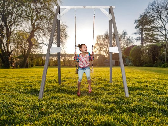 Meisje met gekleurde blouse en spijkerbroek, zittend op een schommel in een tuin.