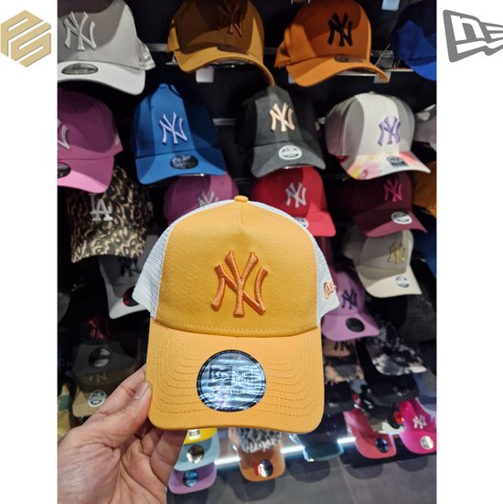 Main tenant une casquette trucker New Era orange avec logo NY Yankees, côtés en mesh blanc.
