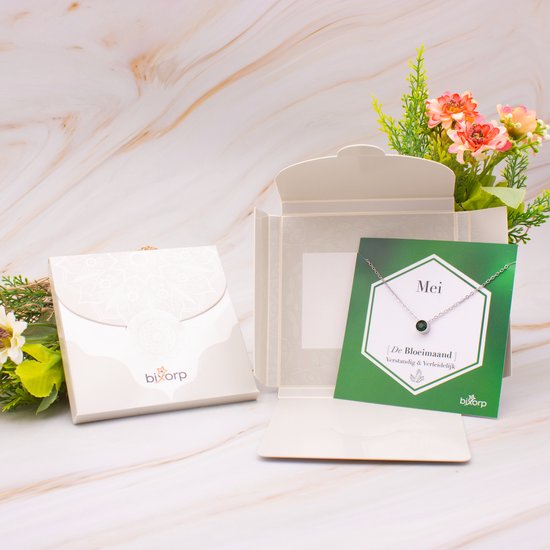 Zilverkleurige ketting met groene zirkonia hanger op een groene kaart in een open gevouwen doos.