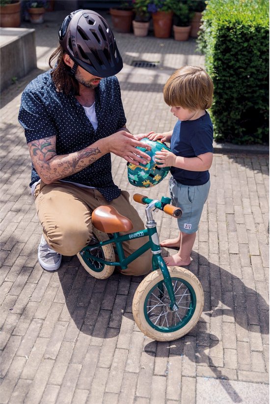 Man met helm en jong kind bij een groene loopfiets.