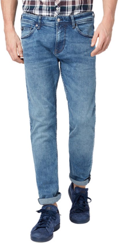Man in een blauwe jeans met opgerolde broekspijpen, gedragen met een geruit shirt en blauwe sneakers.