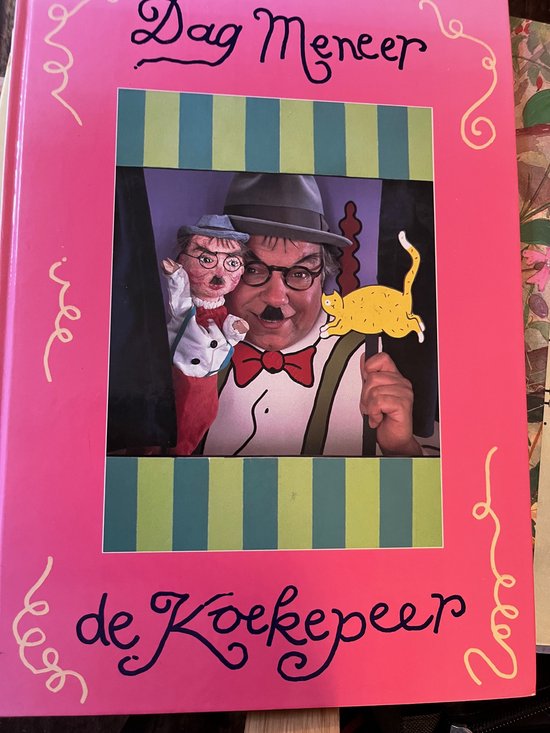 Een man met een hoed en vlinderdas, lachend met een poppenkastpop en een gele kat.