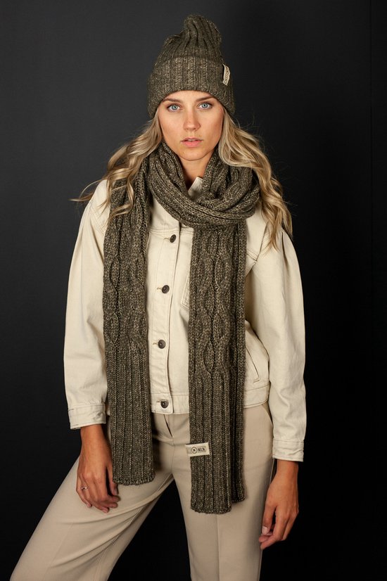 Model met gebreide donkergroene muts en sjaal met kabelpatroon, beige jas en broek.