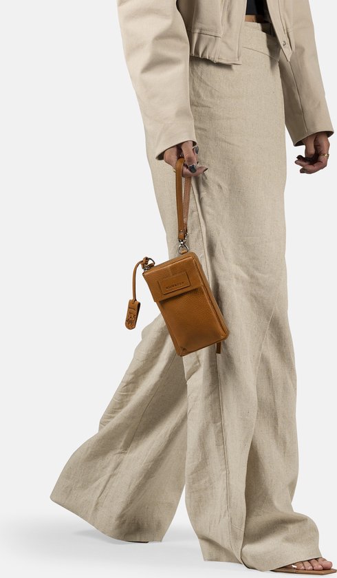 Model dat loopt met een cognac gekleurde telefoonportemonnee met lange schouderband, gedragen bij een beige outfit.