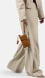 Model dat loopt met een cognac gekleurde telefoonportemonnee met lange schouderband, gedragen bij een beige outfit.