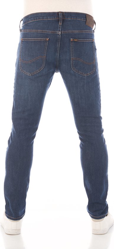 Achterkant van een man in een donkerblauwe jeans met oranje stiksels en een bruin Lee-label.