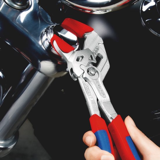 Hand houdt een tang met rode en blauwe handvatten vast, die een deel van een motorfiets aanpast.