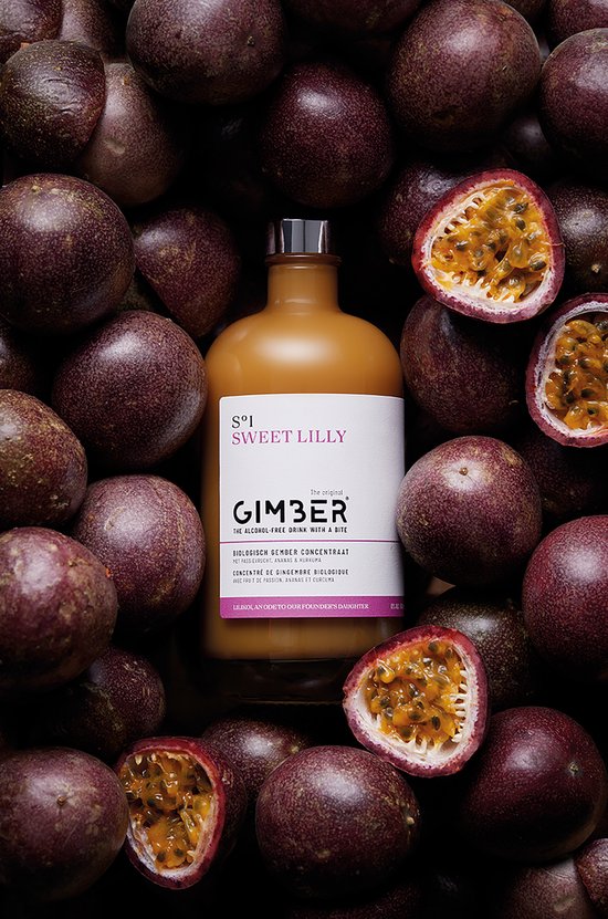 Een fles GIMBER Sweet Lilly in een bed van passievruchten. Biologisch gemberconcentraat met passievrucht, ananas en kurkuma.