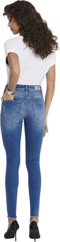 Achterkant van een vrouw in blauwe skinny jeans met rafelige zoom en een witte top, gedragen met zwarte pumps.