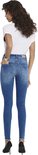 Achterkant van een vrouw in blauwe skinny jeans met rafelige zoom en een witte top, gedragen met zwarte pumps.