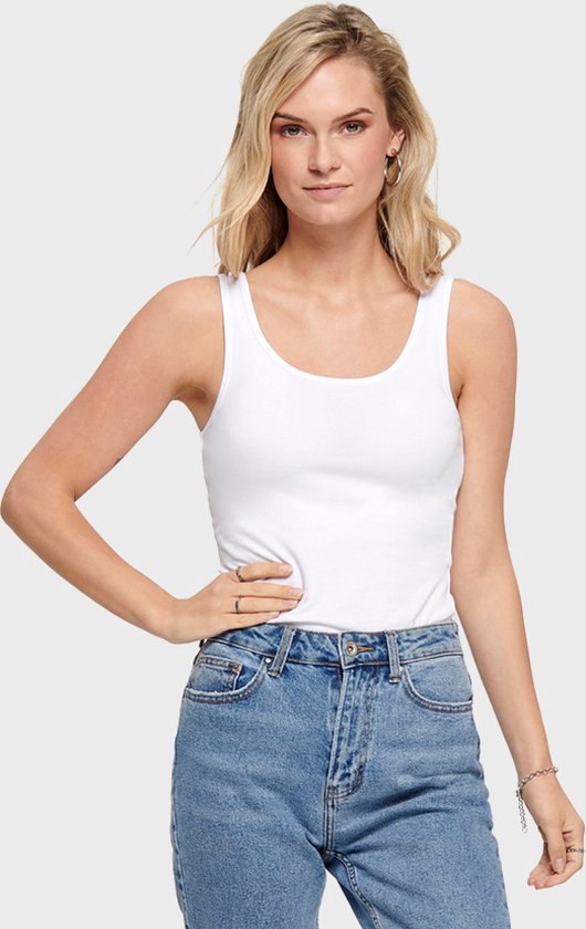 Model met een witte mouwloze top, gecombineerd met een spijkerbroek.