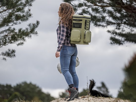 Vrouw met krullend bruin haar, draagt olijfgroene Petromax koelrugzak tijdens een wandeling in de natuur.