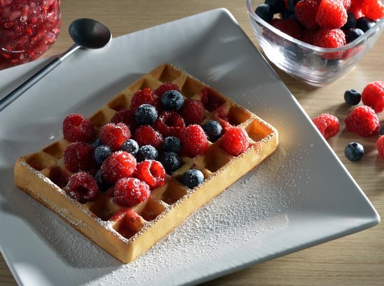 Wafel bestrooid met poedersuiker, belegd met verse frambozen en blauwe bessen.