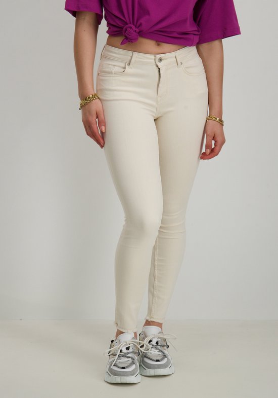 Model in crème skinny jeans en paarse top, met sneakers.