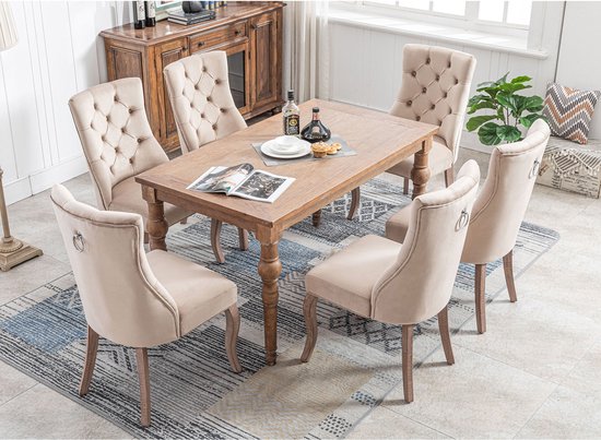 Zes beige fluwelen eetkamerstoelen met hoge rugleuning rond een houten tafel.