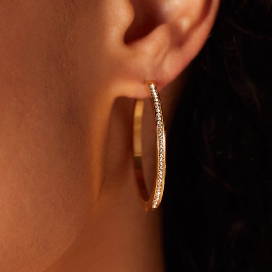 Gouden hoepeloorbel met kristallen, gedragen door een model.