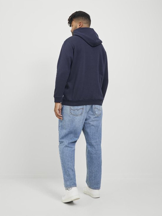 Man met dreadlocks, gekleed in een donkerblauwe hoodie met trekkoord en een spijkerbroek, van achteren gezien.