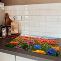 Een kookplaatafdekking met een veld vol kleurrijke klaprozen op een aanrecht naast een inductiekookplaat.