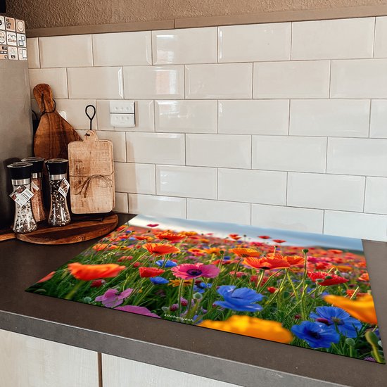 Een kookplaatafdekking met een veld vol kleurrijke klaprozen op een aanrecht naast een inductiekookplaat.