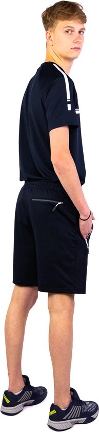 Jonge man in een zwarte tennisoutfit, staand, met t-shirt en short.