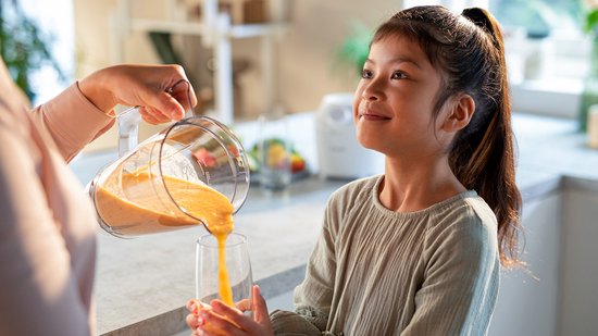 Kind kijkt toe hoe smoothie uit kan wordt geschonken.