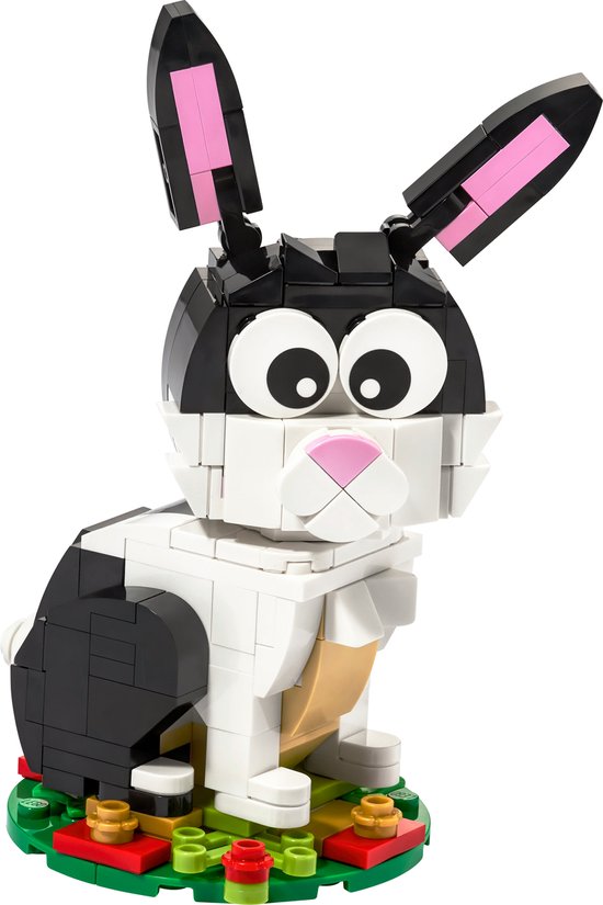 Un lapin LEGO en briques noires, blanches et beiges, avec de grands yeux et l'intérieur rose des oreilles, assis sur une base verte avec des fleurs.
