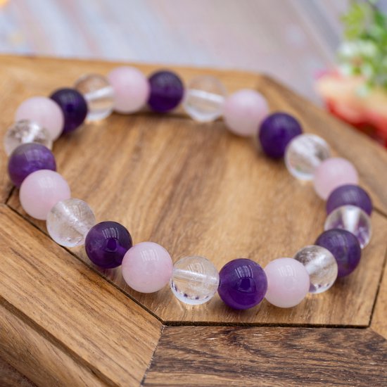 Edelsteenarmband met paarse amethist, roze rozenkwarts en heldere bergkristallen op houten ondergrond.