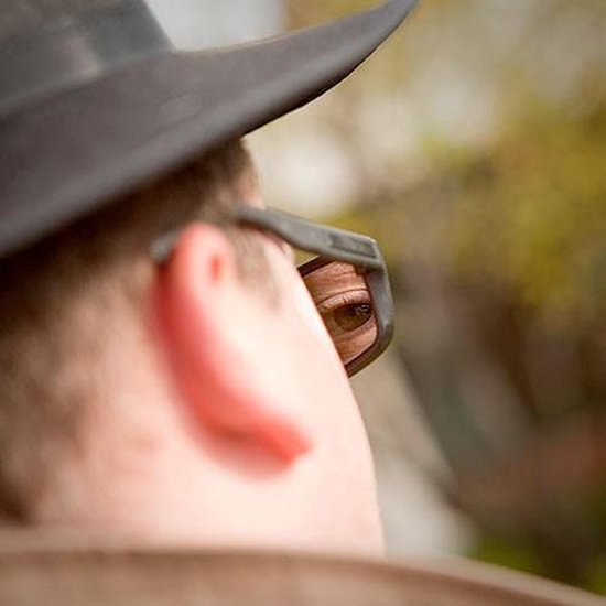 Oog van een persoon dat in de spiegelende lens van een zwarte spionagebril kijkt.
