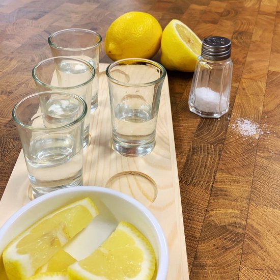 Plateau en bois avec quatre verres à shot, citron, tranches et salière sur fond en bois.